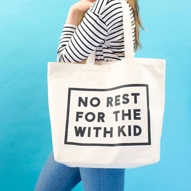Person Carrying a Canvas Tote Bag with ‘No Rest For With the Kid’ Text on a Blue Background