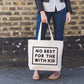 Person Carrying a Canvas Tote Bag with ‘No Rest For With the Kid’ Text on a Neutral Background