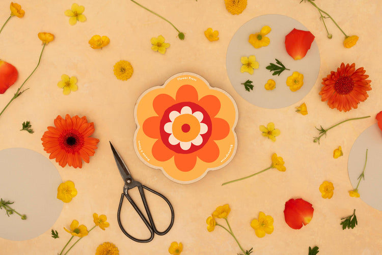 Pocket flower press that is a perfect size to press and dry flowers on the go. Flower-shaped in orange qnd yellow.. Strong elastic bands, 6 sheets of corrugated card and 10 sheets of sugar paper to ensure good pressing. 
