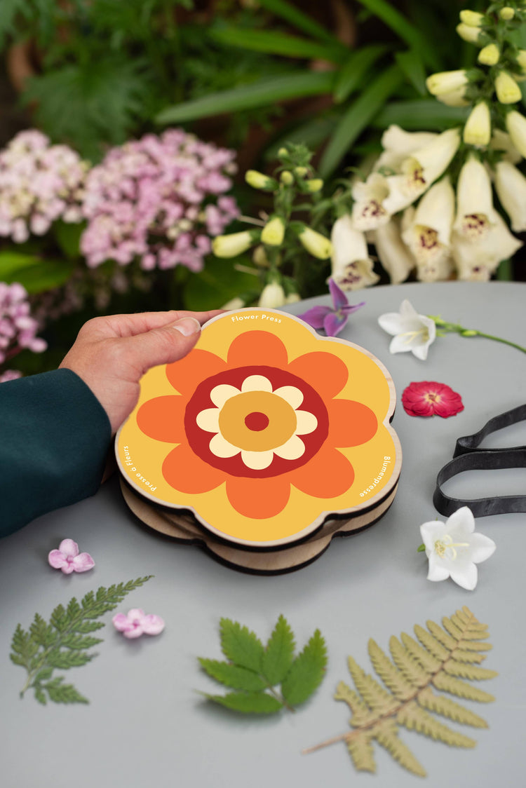 Pocket flower press that is a perfect size to press and dry flowers on the go. Flower-shaped in orange qnd yellow.. Strong elastic bands, 6 sheets of corrugated card and 10 sheets of sugar paper to ensure good pressing. 