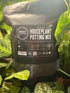 A 3L black resealable pouch of Urban Tropicanas Houseplant Potting Mix, surrounded by green houseplant leaves.