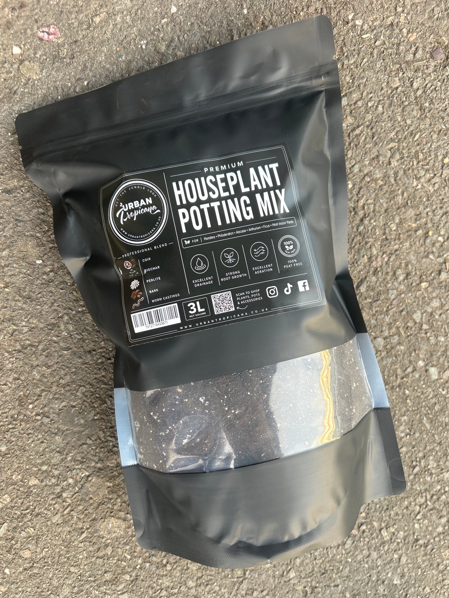 A black resealable pouch of houseplant potting mix by Urban Tropicana placed on a grey asphalt surface. The front label reads &