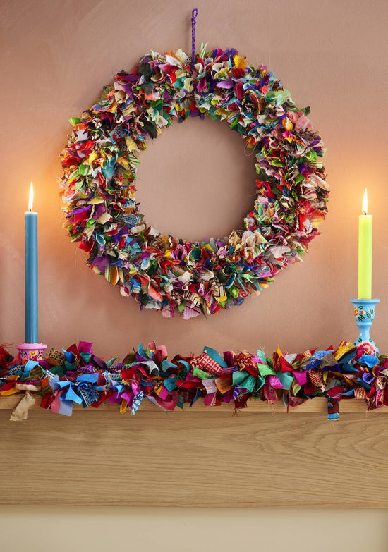 Colorful fabric wreath and garland on a fireplace mantle with candles.