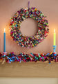 Colorful fabric wreath and garland on a fireplace mantle with candles.
