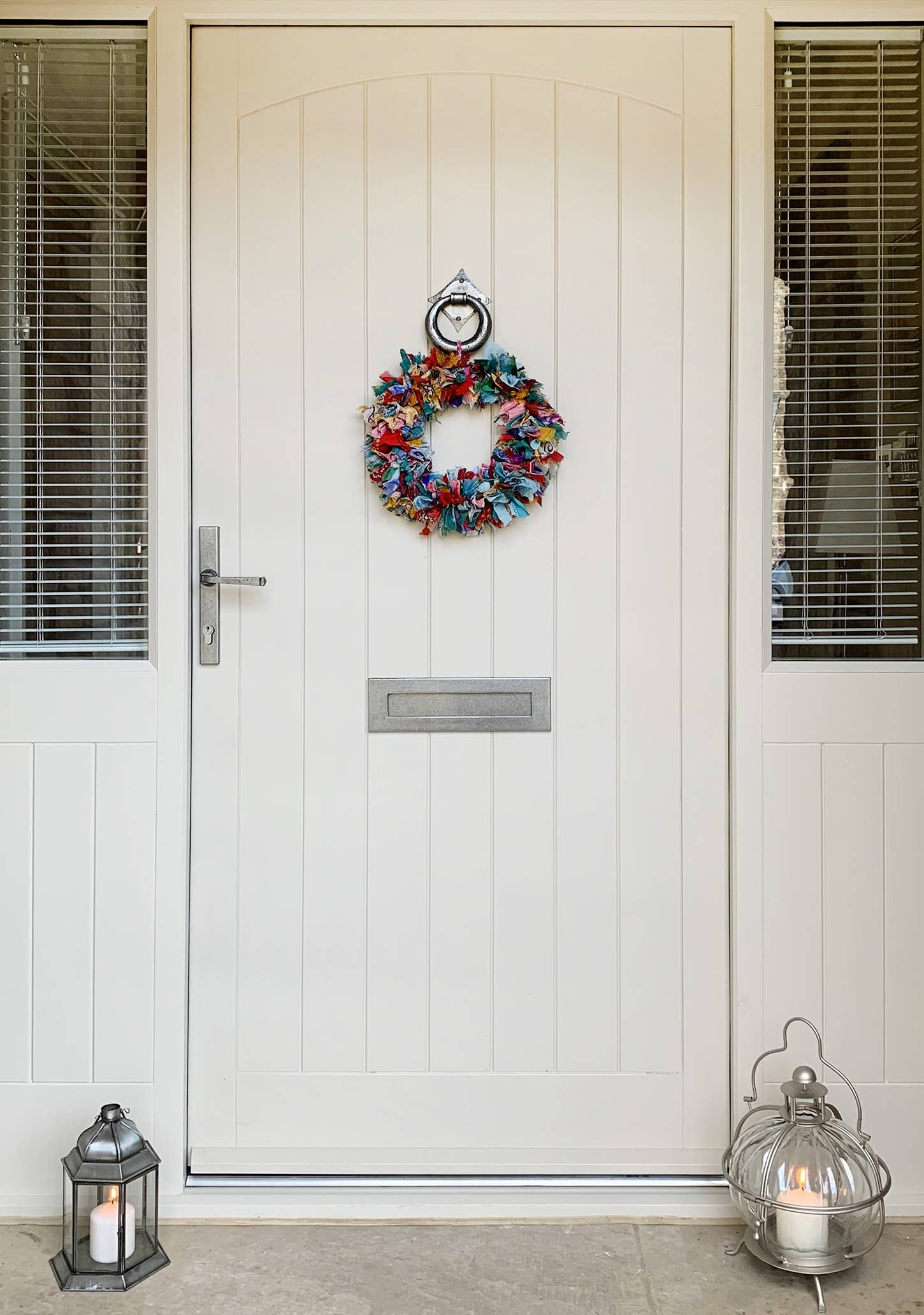 White door with a colorful wreath and lanterns on either side.