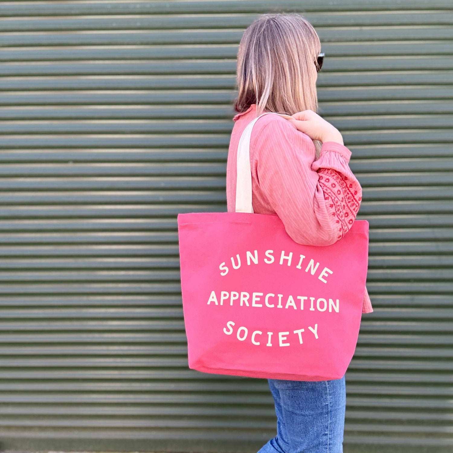 Person Carrying a Bright Pink Canvas Tote Bag with ‘Sunshine Appreciation Society’ text on Green Background