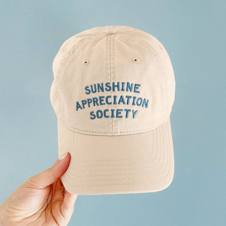 Off-White Cotton Baseball Cap with ‘Sunshine Appreciation Society’ text on a Neutral Background