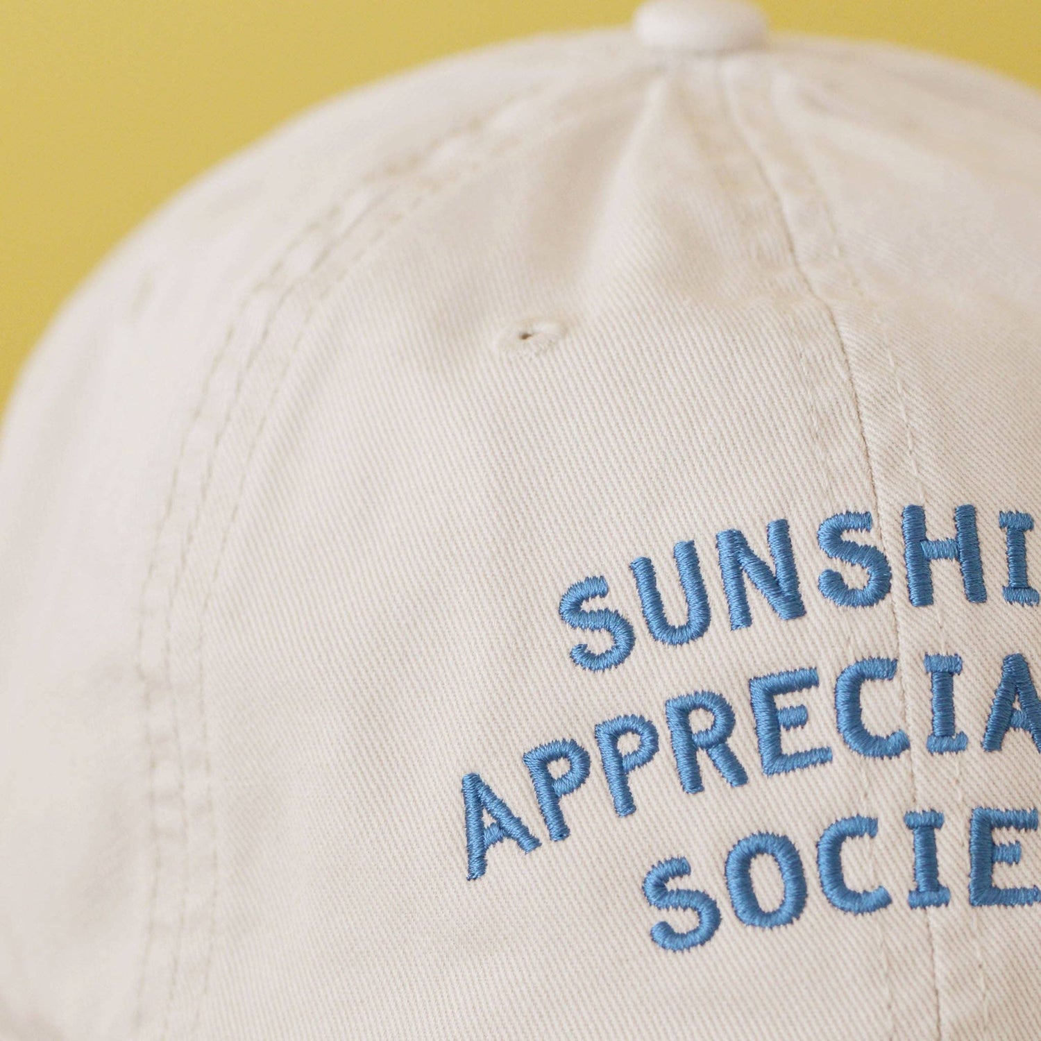 Off-White Cotton Baseball Cap with ‘Sunshine Appreciation Society’ text on a Neutral Background