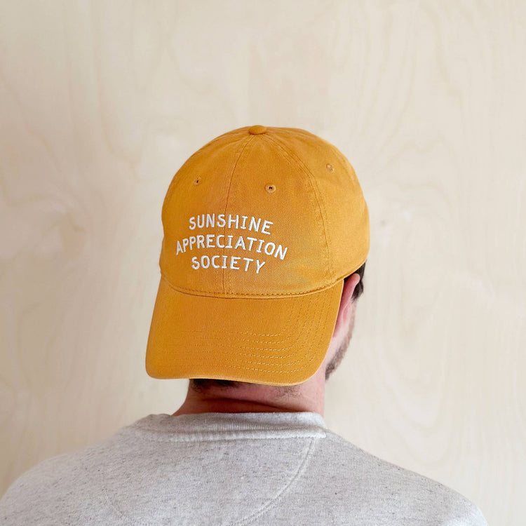 Person Wearing a Cotton Baseball Cap with ‘Sunshine Appreciation Society’ text on a White Background
