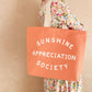 Person Carrying a Peach Canvas Tote Bag with ‘Sunshine Appreciation Society’ text on a Neutral Background