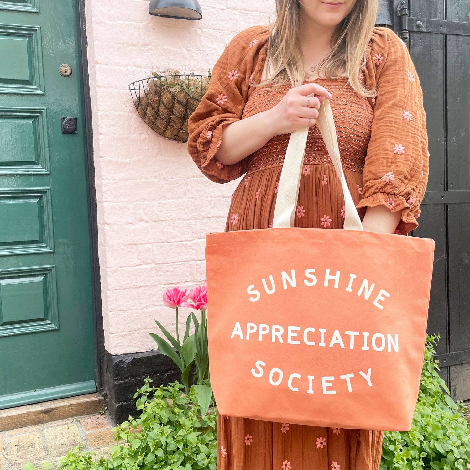 Person Carrying a Peach Canvas Tote Bag with ‘Sunshine Appreciation Society’ text on a Mixed Background