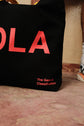 Black reusable canvas tote bag with yellow handles and bold red "Hola" and ‘Adiós’ graphic by The General Classification. Eco-friendly cotton shopping bag with modern minimalist design, ideal for everyday use, groceries, travel, and casual fashion.