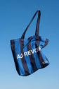 Blue and navy stripe reusable canvas tote bag with navy handles and bold white "Bonjour" and ‘Au Revoir’ graphic by The General Classification. Eco-friendly cotton shopping bag with modern minimalist design, ideal for everyday use, groceries, travel, and casual fashion.