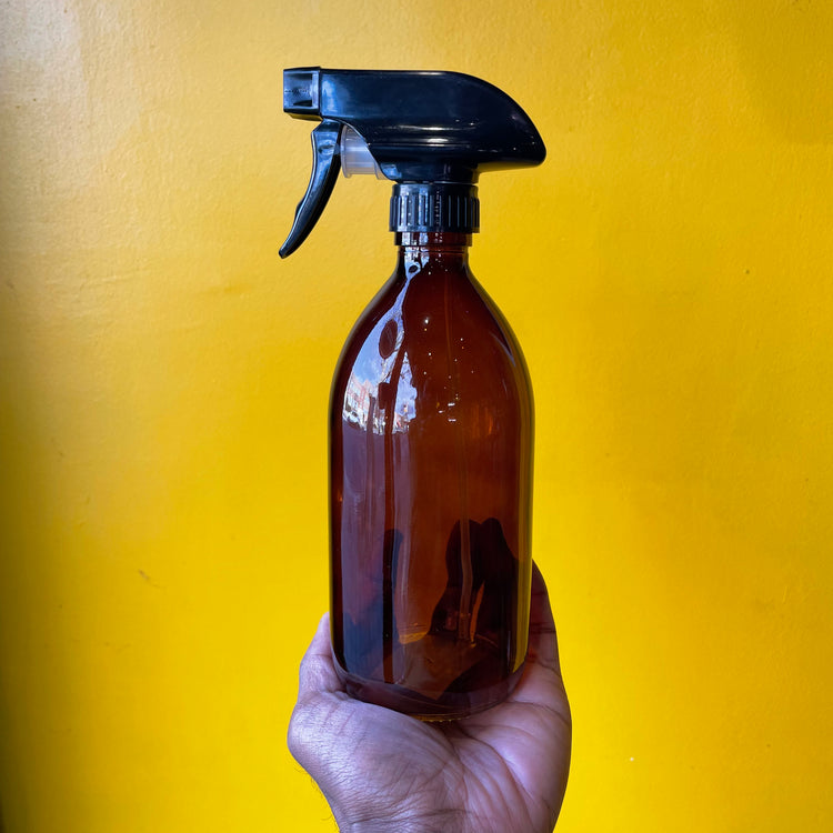 A Amber Glass Refillable Bottle with Spray in front of a yellow background